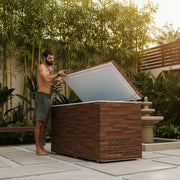 Man opening a wooden cold plunge with a white interior on a patio.