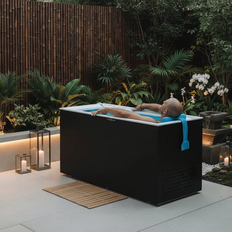 Person lying in a modern outdoor cold plunge tub with plants and a wooden deck in the background