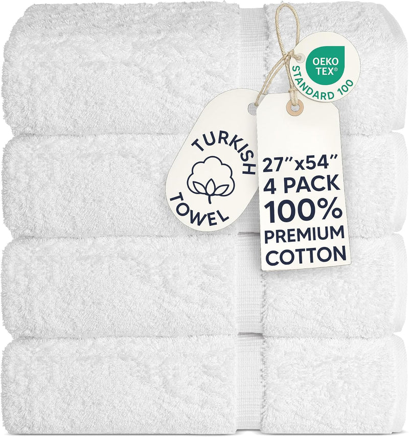 A stack of four folded white Turkish towels with attached paper tags, including an OEKO-TEX Standard 100 badge and a size/quality tag reading 27"x54" 4 PACK 100% PREMIUM COTTON.